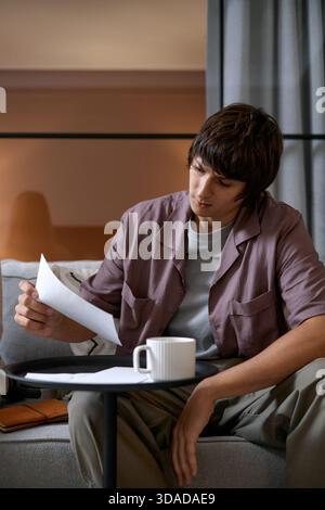 Young Man Reviewing Documents While Sitting Indoors on Sofa Stock Photo