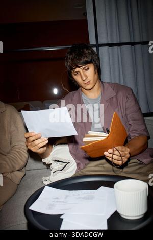 Young Man Reviewing Documents While Sitting Indoors at Night Stock Photo