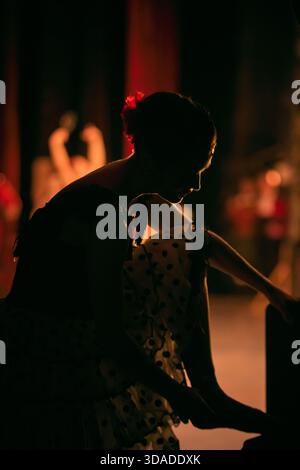 Ballerina adjusting pointe shoes in dim backstage light before stage entry. Stock Photo
