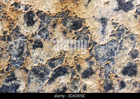 Abstract texture background featuring rough surface pattern of brown and black stone. Gold and yellow detail on mineral creates weathered, rustic feel Stock Photo