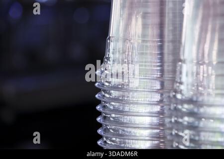 Close up detail of stack of clear transparent plastic disposable cups with repeating pattern. empty drinkware items sit organized against dark backgro Stock Photo