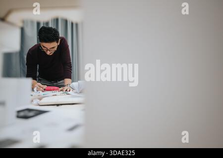 Man leaning over a desk while writing and reviewing documents in a modern collaboration workspace Stock Photo