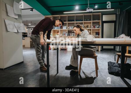 Two students collaborate at a design studio table, reviewing plans in a modern collaboration center. Stock Photo