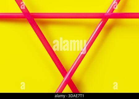 Three pink plastic drinking straws arranged in triangle, closeup detail over yellow background Stock Photo