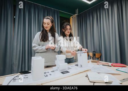 Two students collaborate at a design studio, arranging white architectural models and planning a project in a modern collaboration center Stock Photo