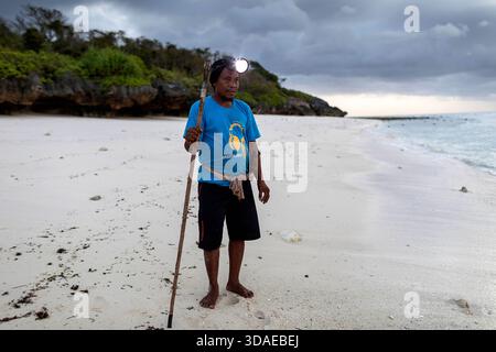 A local fisherman with a headlamp and spear preparing for a night reef fishing trip under a dramatic storm sky on Sumba Island, Indonesia. Stock Photo