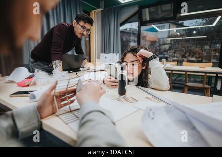 Students collaborate at a workshop table, using laptops and phones during a group study session Stock Photo