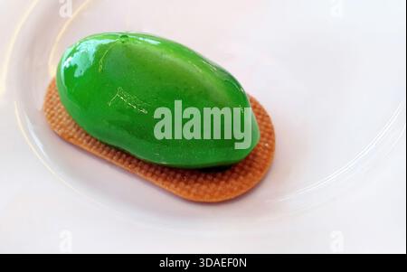 High angle close up view of an elegant green mousse cake with a shiny mirror glaze finish. The oval-shaped dessert rests on a crispy textured biscuit Stock Photo