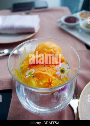 Refreshing mango or passion fruit sorbet served in a double-layered glass bowl. The bright yellow frozen dessert is beautifully garnished with small w Stock Photo