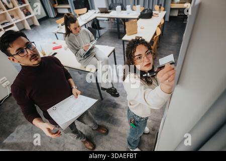 Students collaborate in a modern studio, reviewing blueprints and writing on a whiteboard Stock Photo