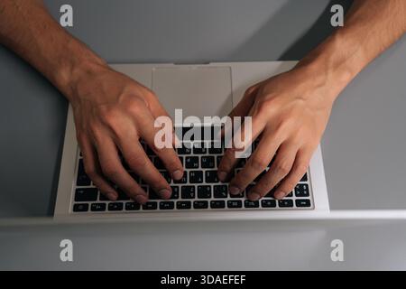 Close-up hands of unrecognizable businessman typing on laptop keyboard, professional home office scene showing remote work, coding, online learning Stock Photo