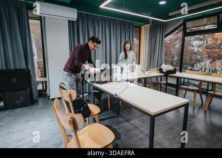 Two students collaborate in a modern classroom workshop space with laptops and materials on a long table Stock Photo