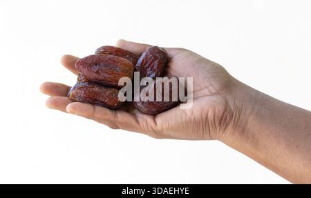 Close-up of a female hand gently holding several fresh Medjool Dates fruit against a white background. Healthy eating, sweet food, commercial concept, Stock Photo