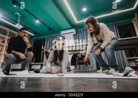 Three students collaborate in a modern studio, reviewing plans and building a model during a group study session Stock Photo