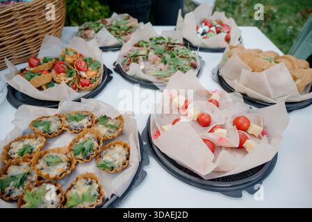 Catering light snacks on a white table outdoors. Organizing a street buffet with mini appetizers on black trays and parchment paper Stock Photo