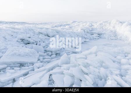 A bright icy shoreline features jagged white ice shards piled along the coast of frozen Baltic Sea. The calm sea and distant horizon evoke cold, isola Stock Photo