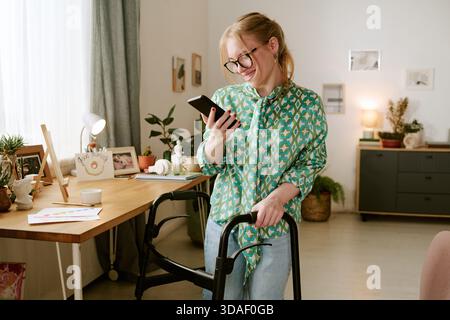 Young Woman with Disability Smiling While Using Smartphone Indoors Stock Photo