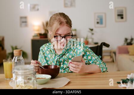 Young Woman with Disability Smiling While Using Smartphone at Breakfast Stock Photo