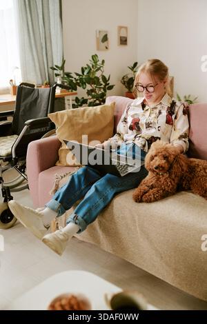 Young Woman Sitting with Disability Using Laptop and Petting Dog Stock Photo