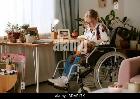 Young Woman with Disability Sitting in Wheelchair Petting Dog Stock Photo