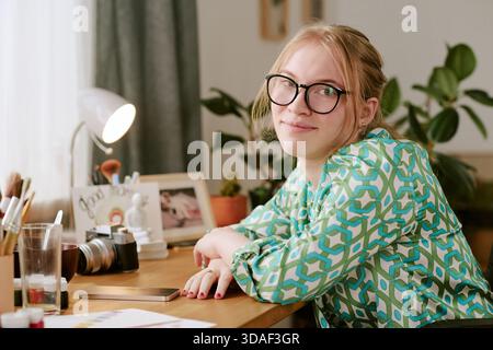 Portrait of Young Adult Woman Smiling While Sitting at Desk Stock Photo