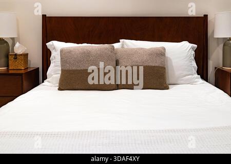 Cozy modern bedroom interior with a wooden headboard, white bedding, and matching neutral accent pillows arranged neatly on the bed Stock Photo