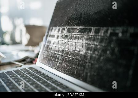 Abandoned laptop displaying a heavily dust-covered screen and the clear reflection of its keyboard, illustrating themes of technological obsolescence, neglect, and forgotten digital items Stock Photo