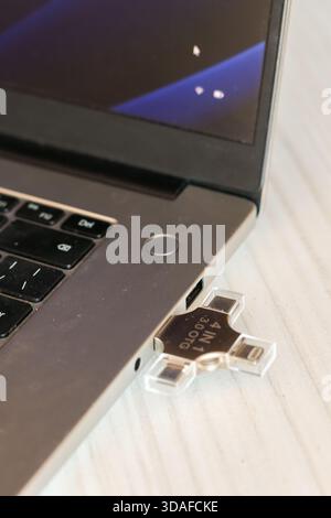 Close-up of a sleek silver laptop connected to a versatile multi-connector USB flash drive on a light wooden table, highlighting data transfer capabil Stock Photo