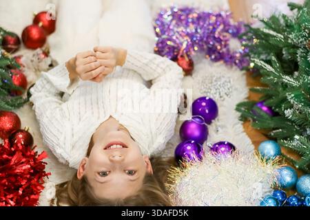 Smiling child in cozy setup with scattered multicolored baubles and garlands Stock Photo
