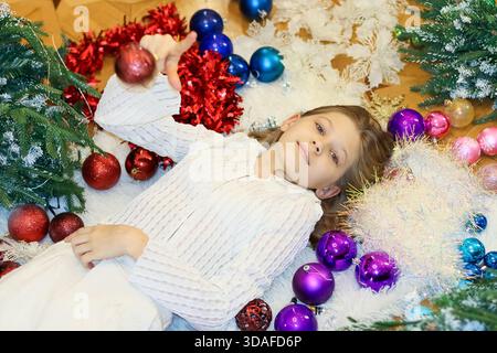 Child in relaxed position on mat with multicolored baubles and tinsel details Stock Photo