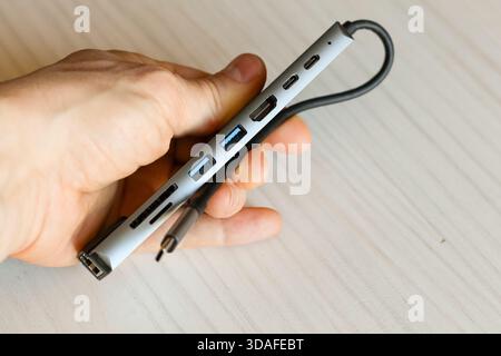 Silver USB-C docking hub with multiple ports including HDMI and USB, held in hand with USB-C cable dangling Stock Photo