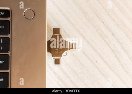 A 4-in-1 USB adapter with USB, USB-C, Lightning, and micro-USB ports in gold finish, placed beside a laptop on a wooden surface for versatile charging Stock Photo