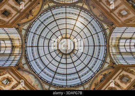 A stunning upward view of a large circular glass dome framed by ornate architectural details. Sunlight filters through the grid, highlighting decorati Stock Photo