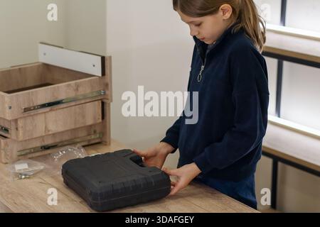 Preteen girl in casual clothes carefully opening black plastic tool case on table during furniture assembly at home Stock Photo