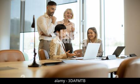 A diverse group of professionals engages in a meeting in a contemporary office setting. They discuss ideas while reviewing materials on laptops in the Stock Photo