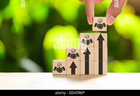 Teamwork and business growth strategy concept. Hand placing wooden blocks with handshake and arrow icons, representing trust, progress and successful Stock Photo