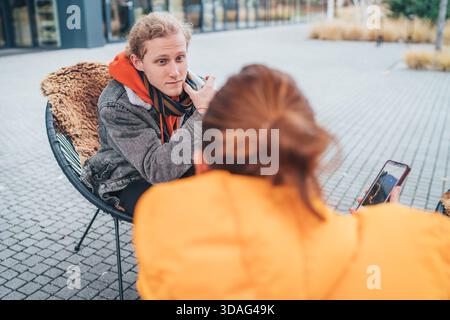 Mother with adult son sitting on an open terrace in a coffee shop, drinking coffee and having a lovely conversation. Mom shows interesting content on Stock Photo