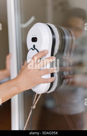 Closeup of housewife mounting high-tech robotic window cleaner on glass surface, utilizing automated cleaning technology for pristine, streak-free Stock Photo