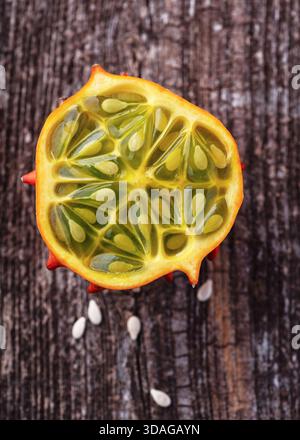 Top view of a sliced horned melon, Kiwano (Cucumis metuliferus) with glossy lime-green interior and translucent seeds on weathered wood. Stock Photo