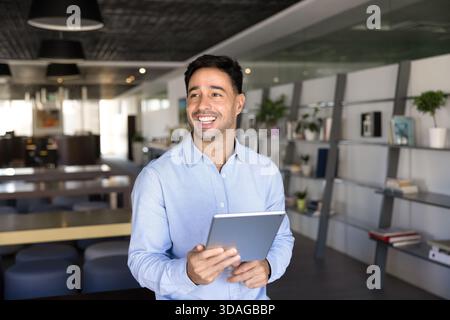 Happy young Hispanic businessman holding digital tablet Stock Photo
