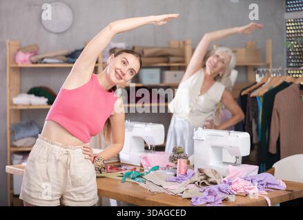 Elderly and adult women doing warm-up exercises in sewing workshop Stock Photo