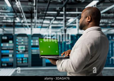 Engineer in server farm using green screen mockup laptop, checking recovery plan. Data center IT expert using chroma key notebook, troubleshooting rigs connectivity issues Stock Photo