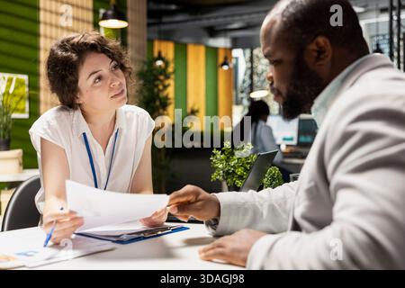 Female HR recruiter speaking with black man job seeker in office, discussing CV resume feedback during formal interview, asking questions to ensure a successful meeting for career development. Stock Photo