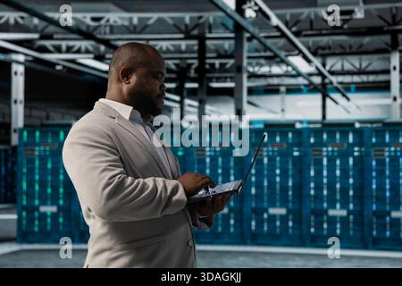 Server farm IT expert doing hardware scans, fixing network issues affecting rigs performance. African american data center admin runs system diagnostic tests on laptop, tracking resource utilization Stock Photo