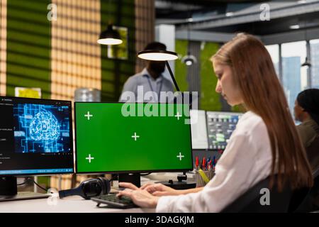 Female engineer developing applications using green screen computer, integrating AI in office systems. Worker doing internship in tech startup debugging applications using chroma key PC Stock Photo