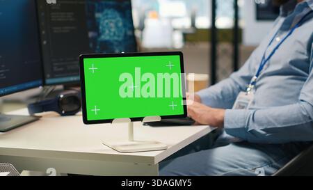 Technician developing applications using chroma key tablet, integrating AI next to office coworkers. Upbeat IT specialist debugging applications with isolated screen device , camera A Stock Photo