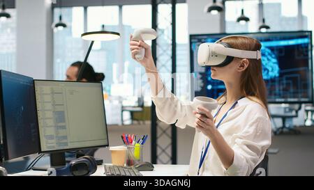 Junior dev using virtual reality at work, testing generative AI machine learning algorithms. Young woman wearing VR goggles equipment scaling productivity with AI large language model code, camera A Stock Photo