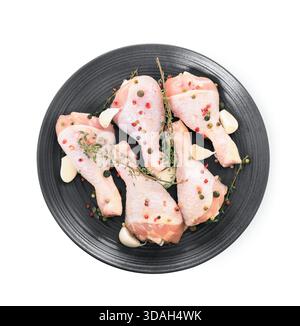 Raw chicken drumsticks on black plate with thyme, garlic and peppercorns isolated on white background. High quality photo Stock Photo