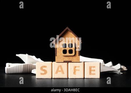 Cubes with word SAFE, house figure and broken pieces on black table. Earthquake concept Stock Photo