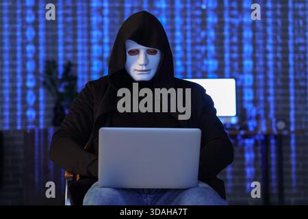 Hacker with laptop sitting in dark room Stock Photo